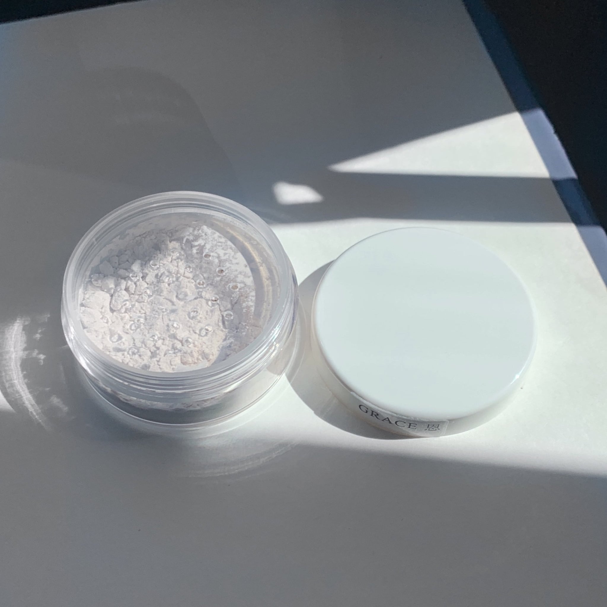Powdered makeup in clear plastic jar with white lid, "GRACE" text visible