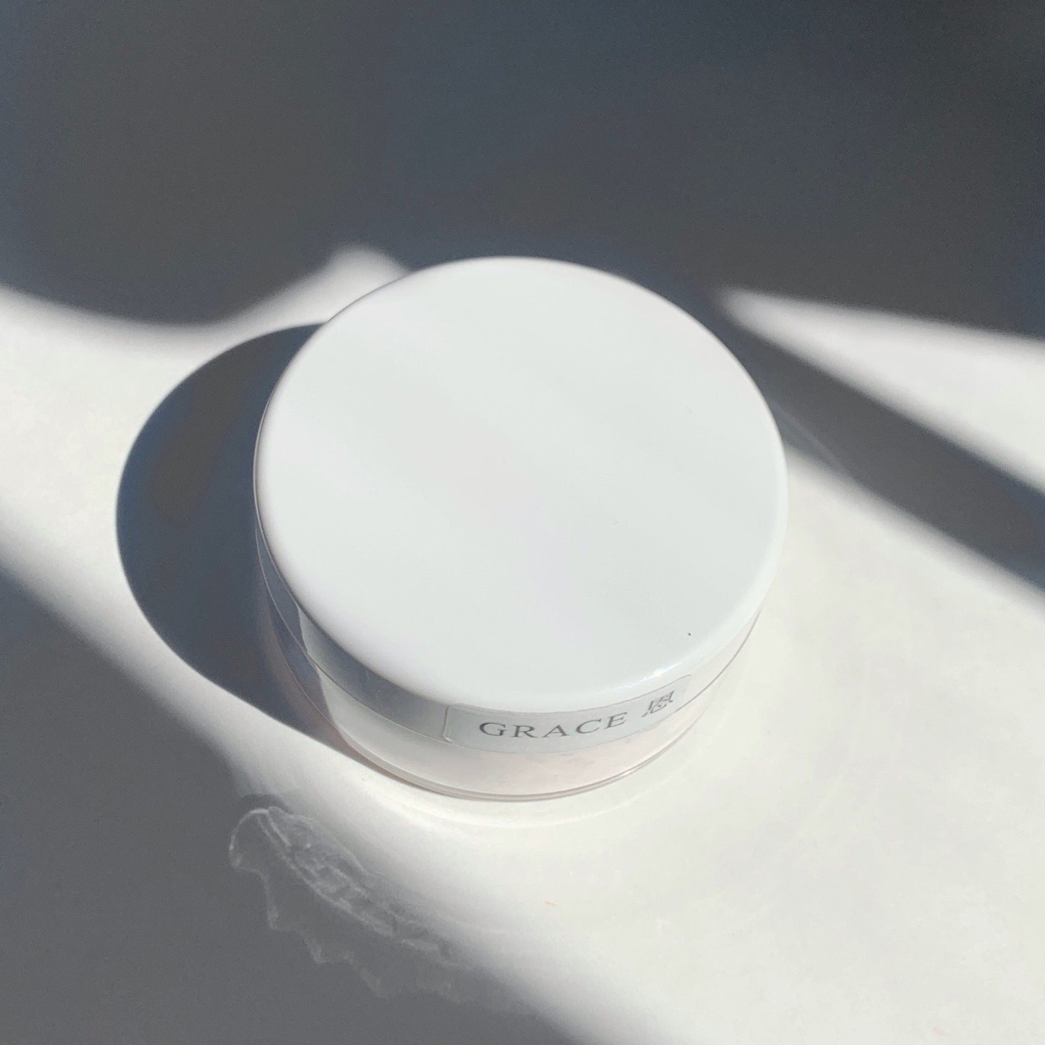 White cosmetic jar with "GRACE" label, round shape, and shadow pattern