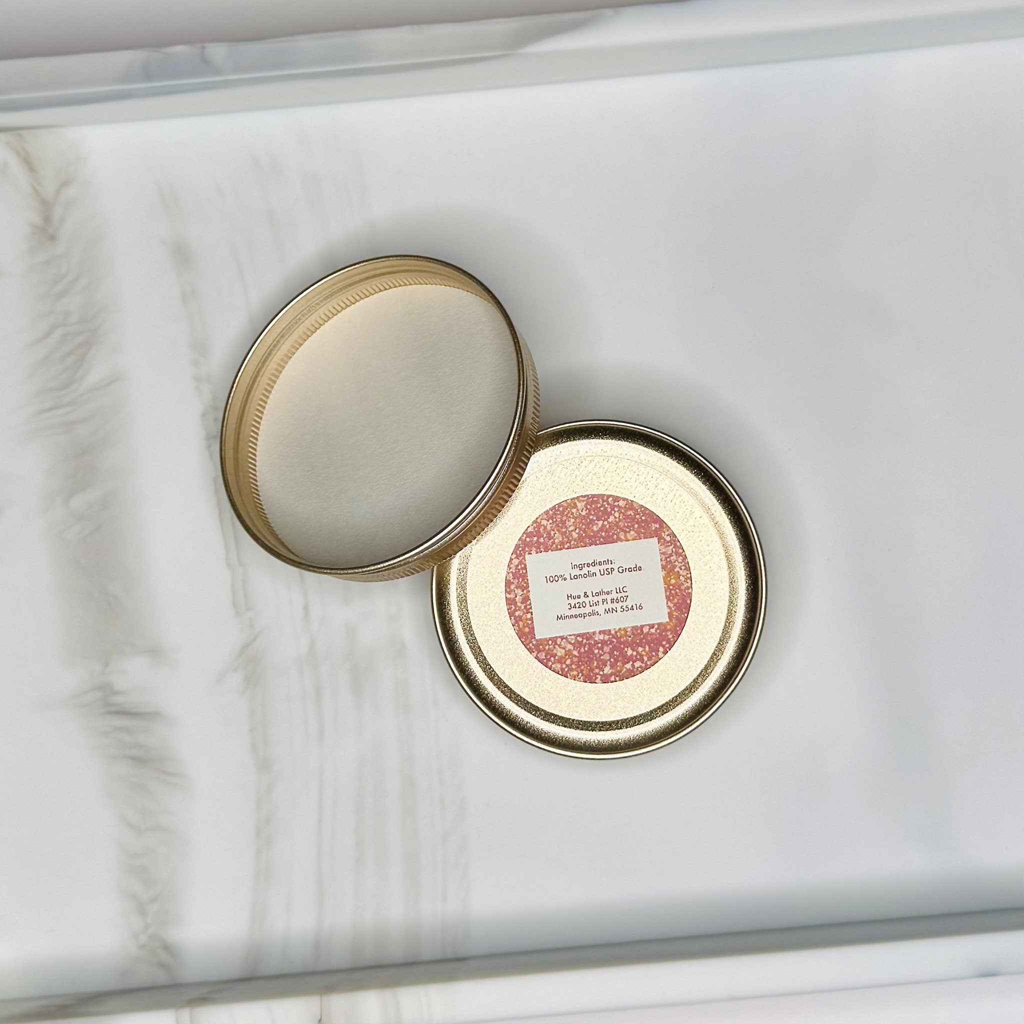 Jar lid with gold rim, pink label, and white interior, Hue & Lather LLC text visible