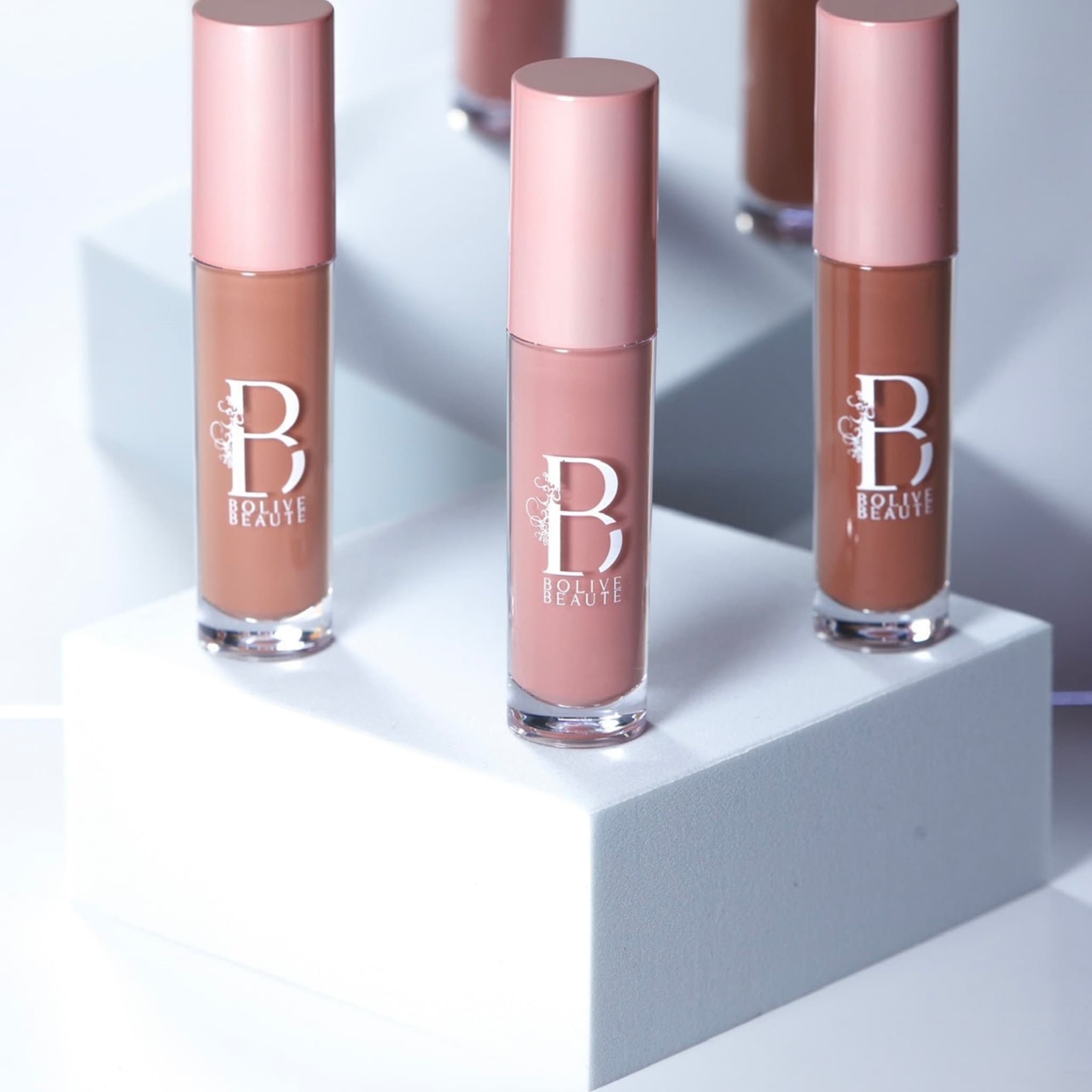 Lip gloss tubes with pink caps and Bolive Beaute logo on a white surface