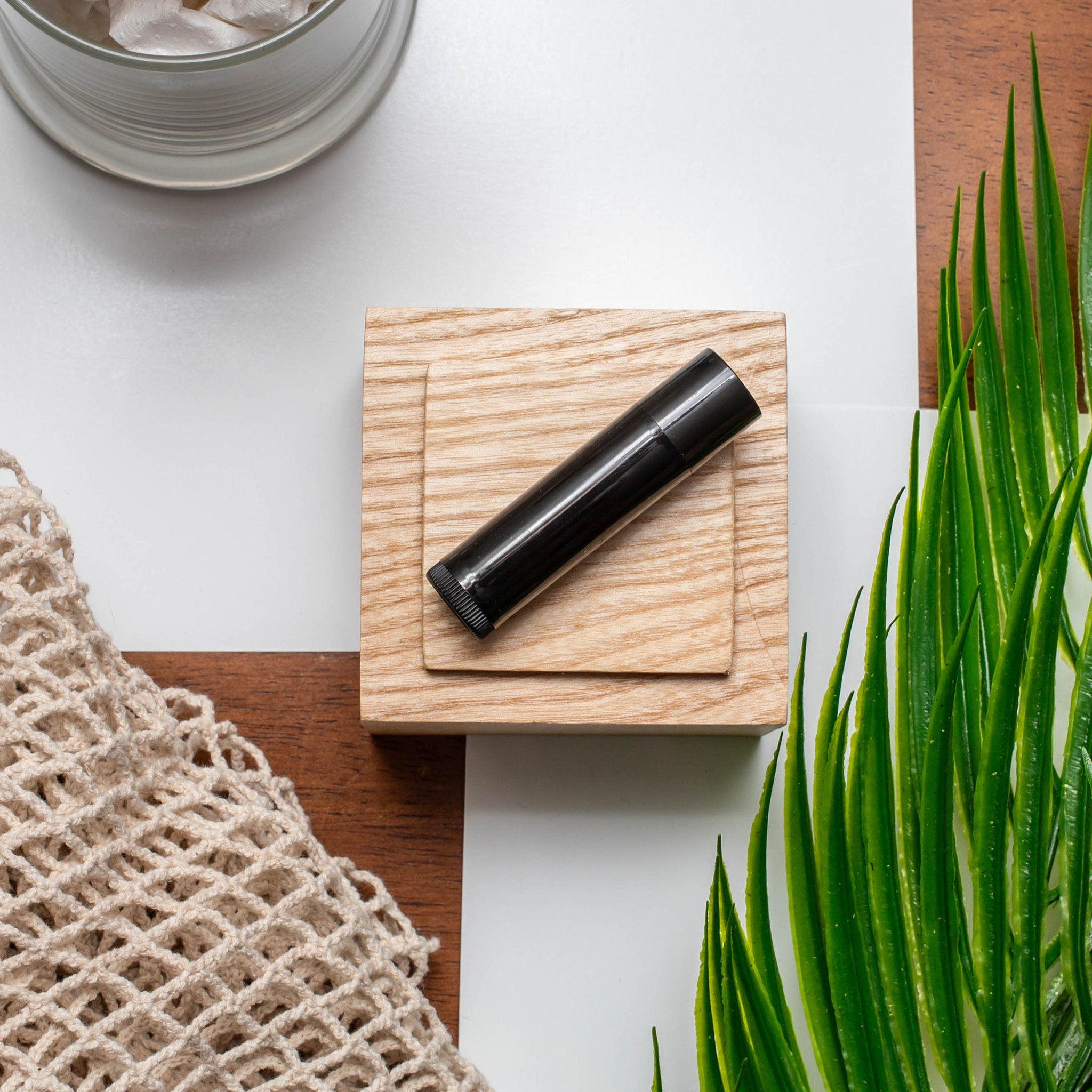 Black tube on wood block, with green leaves and beige net bag, overhead shot
