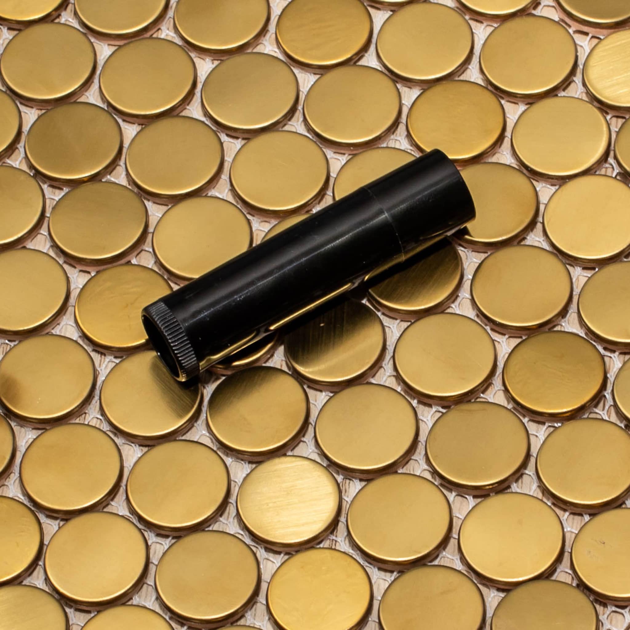 Gold mosaic tile with black cylindrical object, circular pattern, and metallic finish