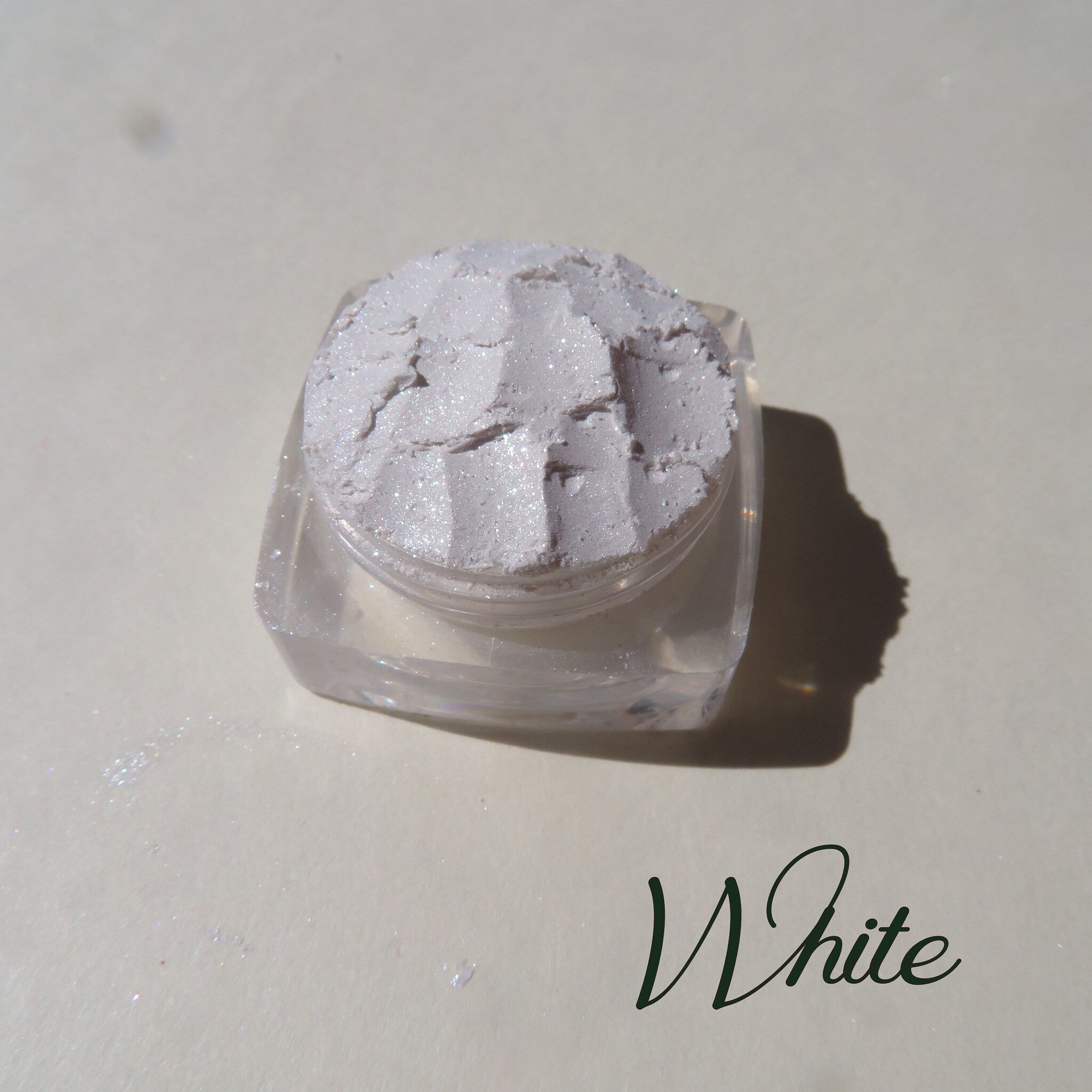 Side view of loose mineral eyeshadow in soft white with shimmer, showcasing powder texture in open jar