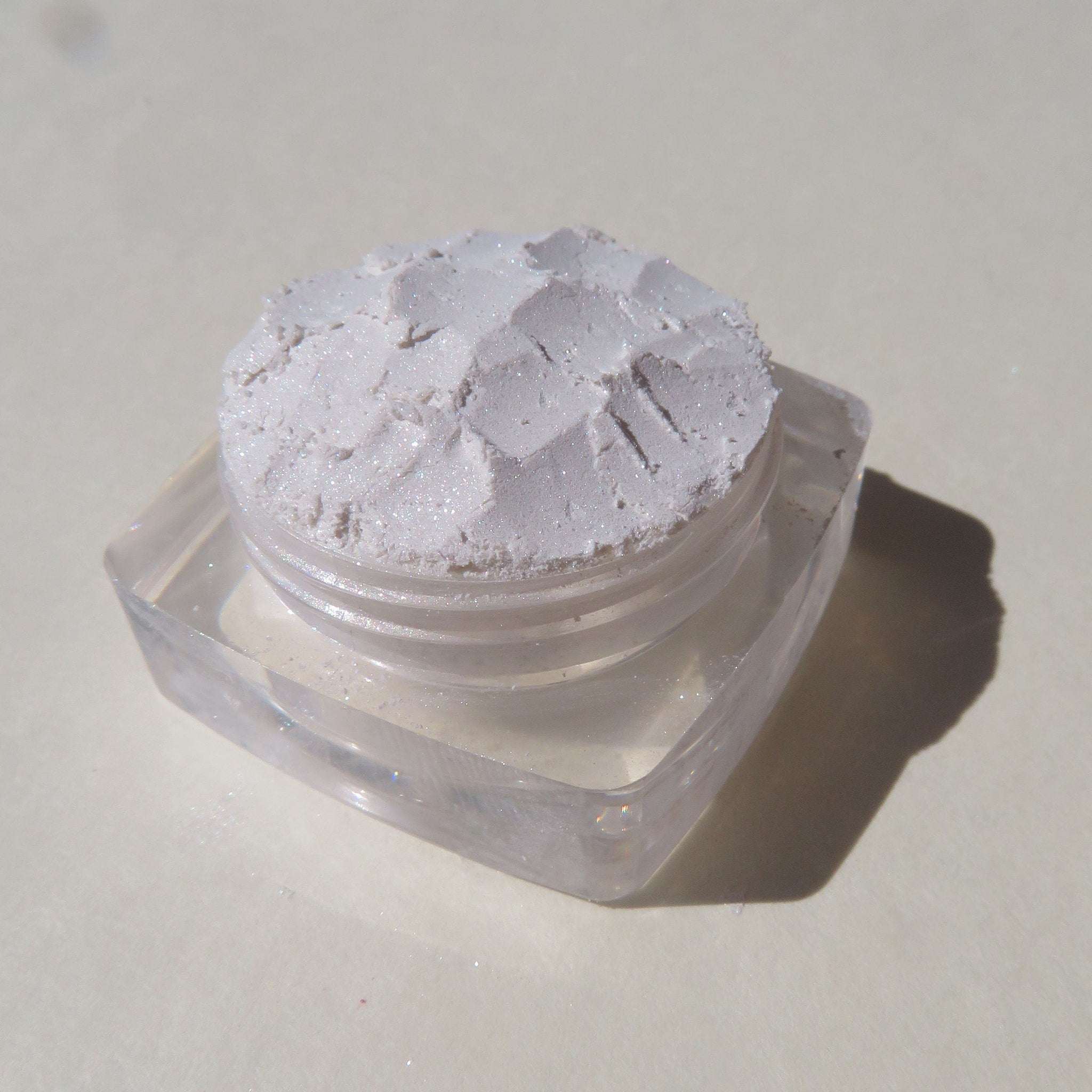 Side view of loose mineral eyeshadow in soft white with shimmer, showcasing powder texture in glass jar
