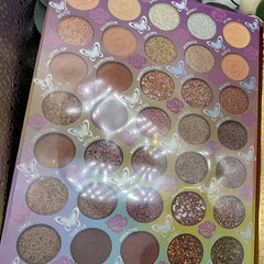 Eyeshadow palette with various shades, glitter, and butterfly accents on a purple background.