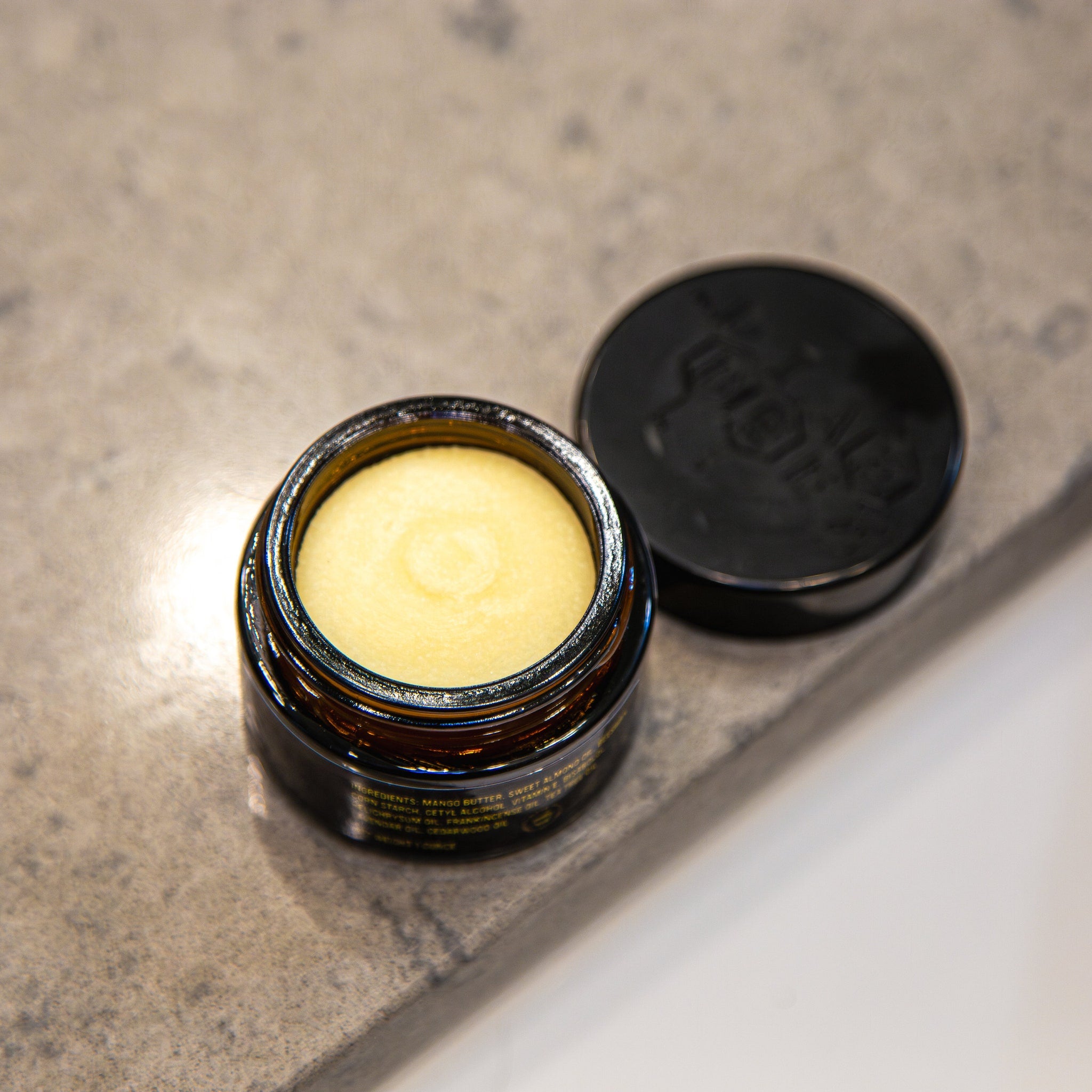Jar of yellow balm in a brown glass jar with black lid on a gray surface