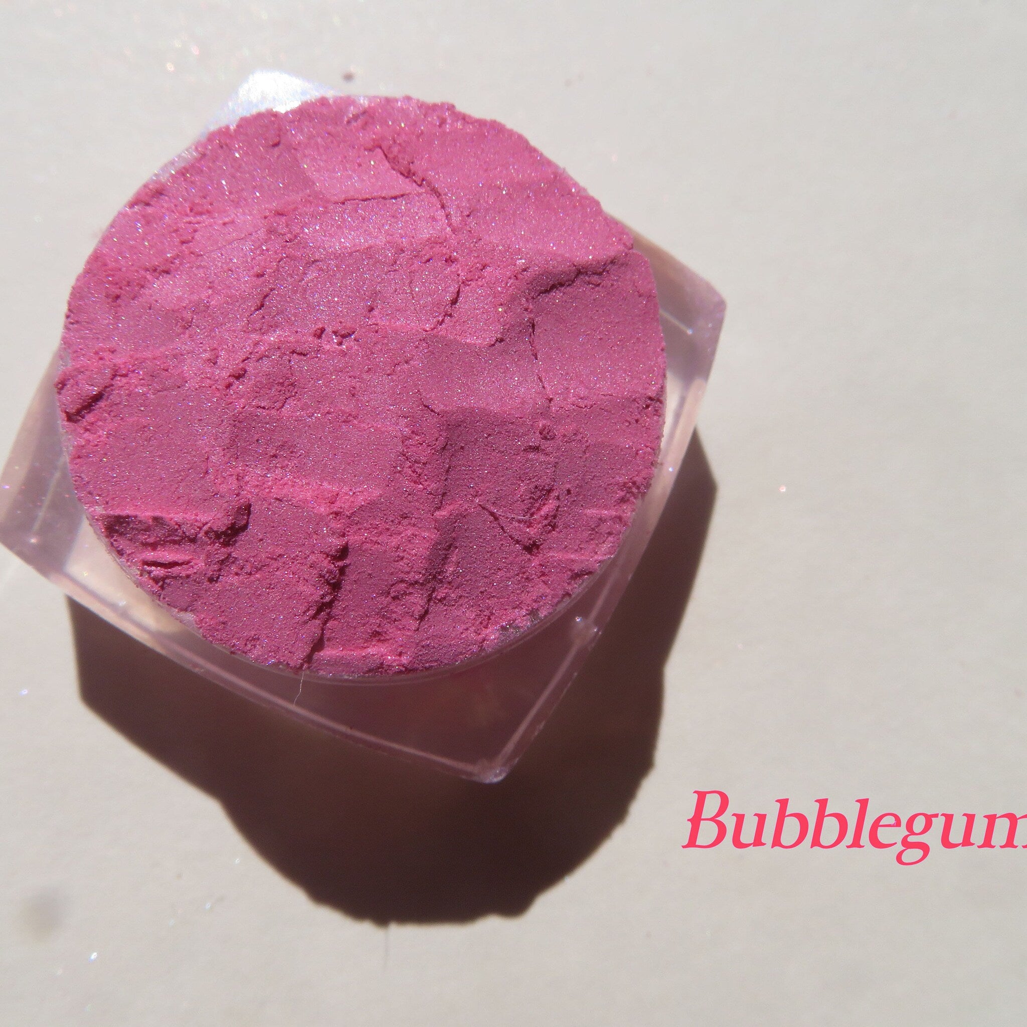 Side view of loose bubblegum pink mineral eyeshadow powder spilling from jar onto marble surface