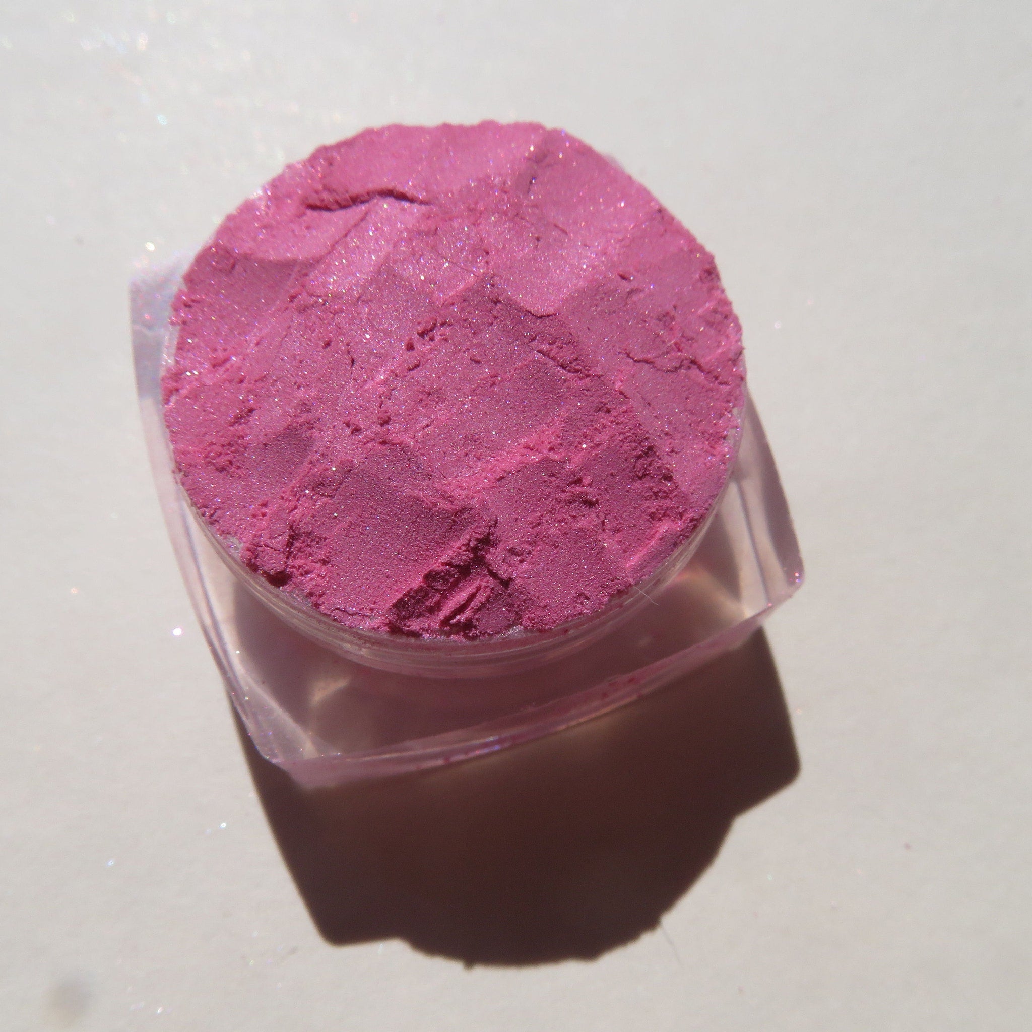 Open jar of soft sheer pink loose mineral eyeshadow with a small brush dipped in pigment