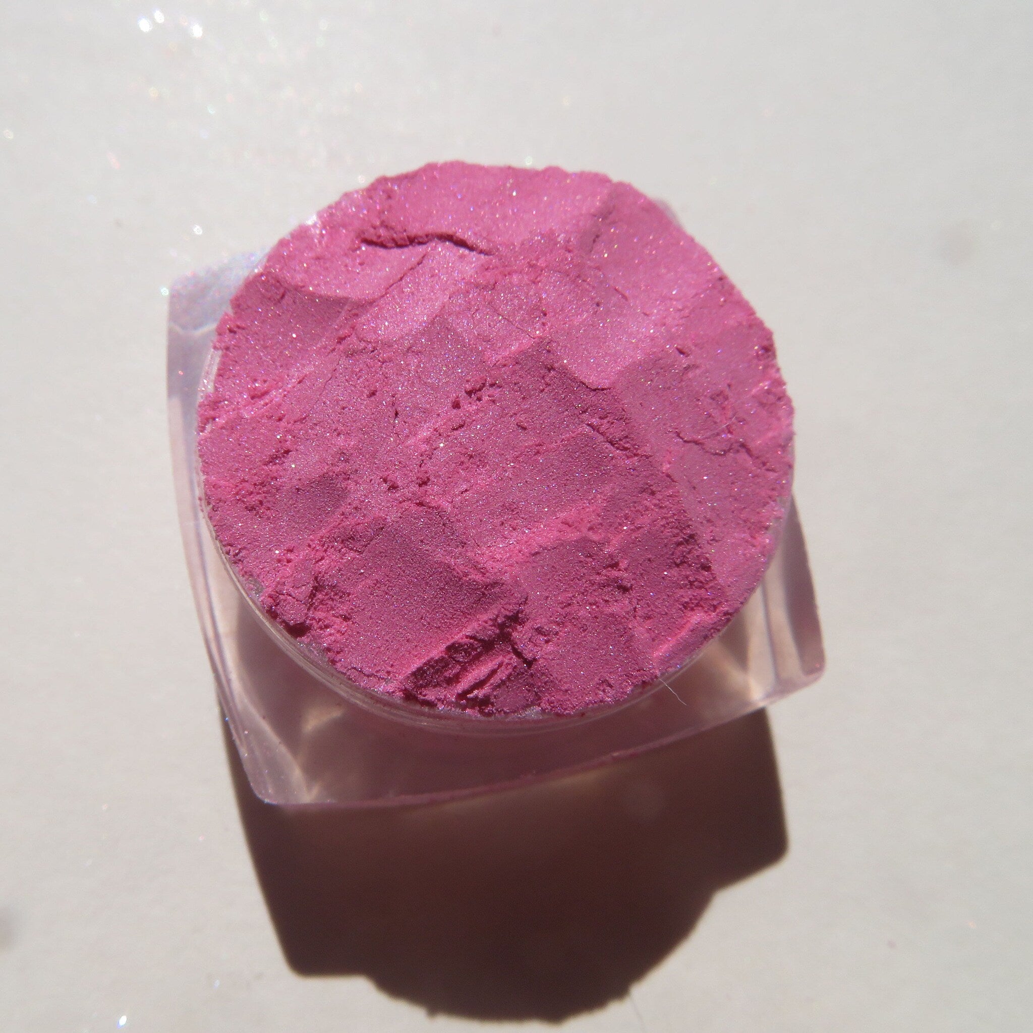 Side view of loose pink mineral eyeshadow powder spilling from jar with soft sheer shimmer