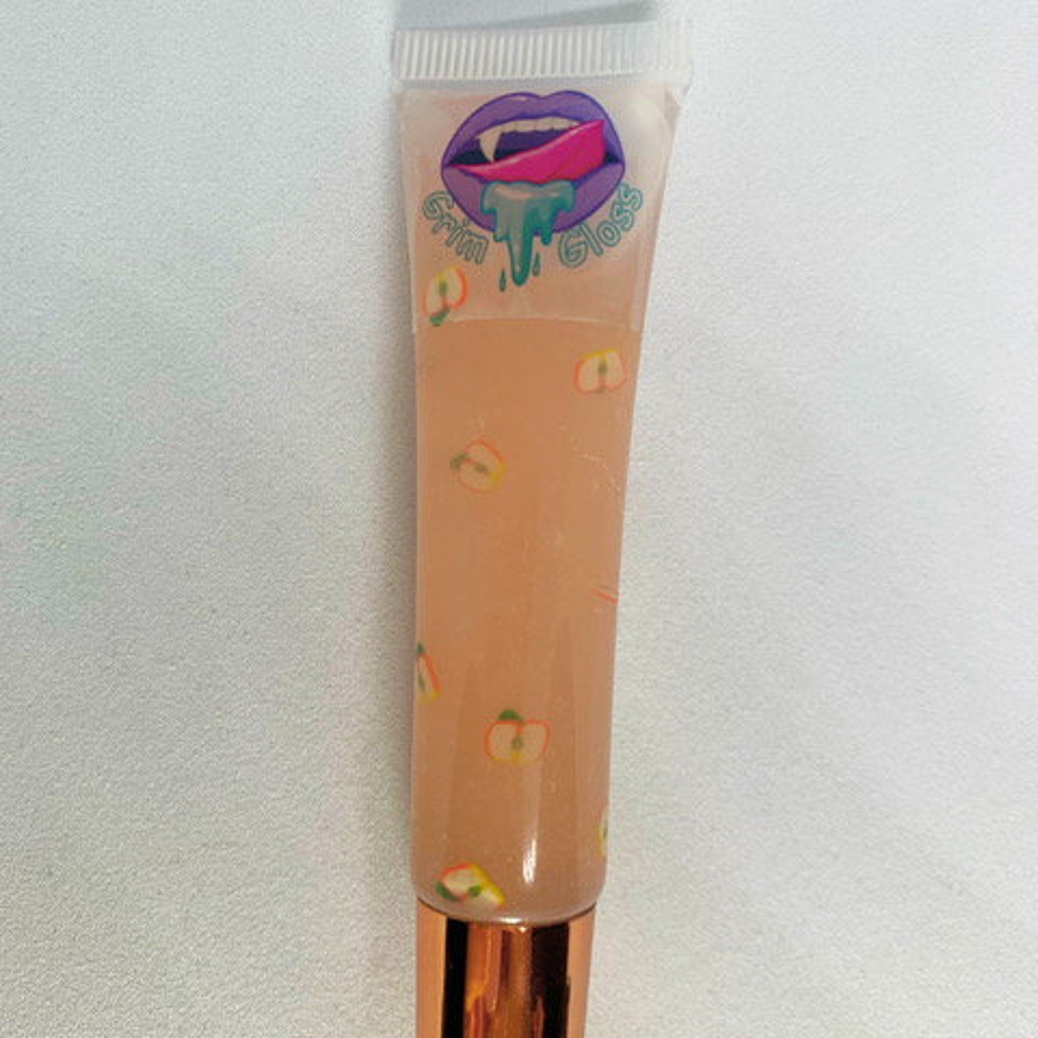 Lip gloss tube with peach colored liquid, apple pattern, and Grim Gloss logo on white background