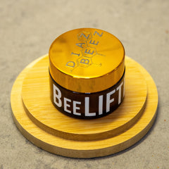 Cosmetic jar with gold lid, brown glass, and "BEE LIFT" text on a wooden stand