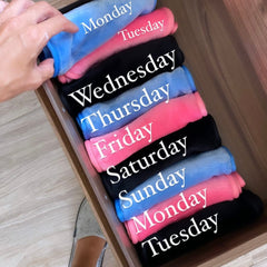 Rolled fabric items in drawer, various colors, labeled with days of the week in white text
