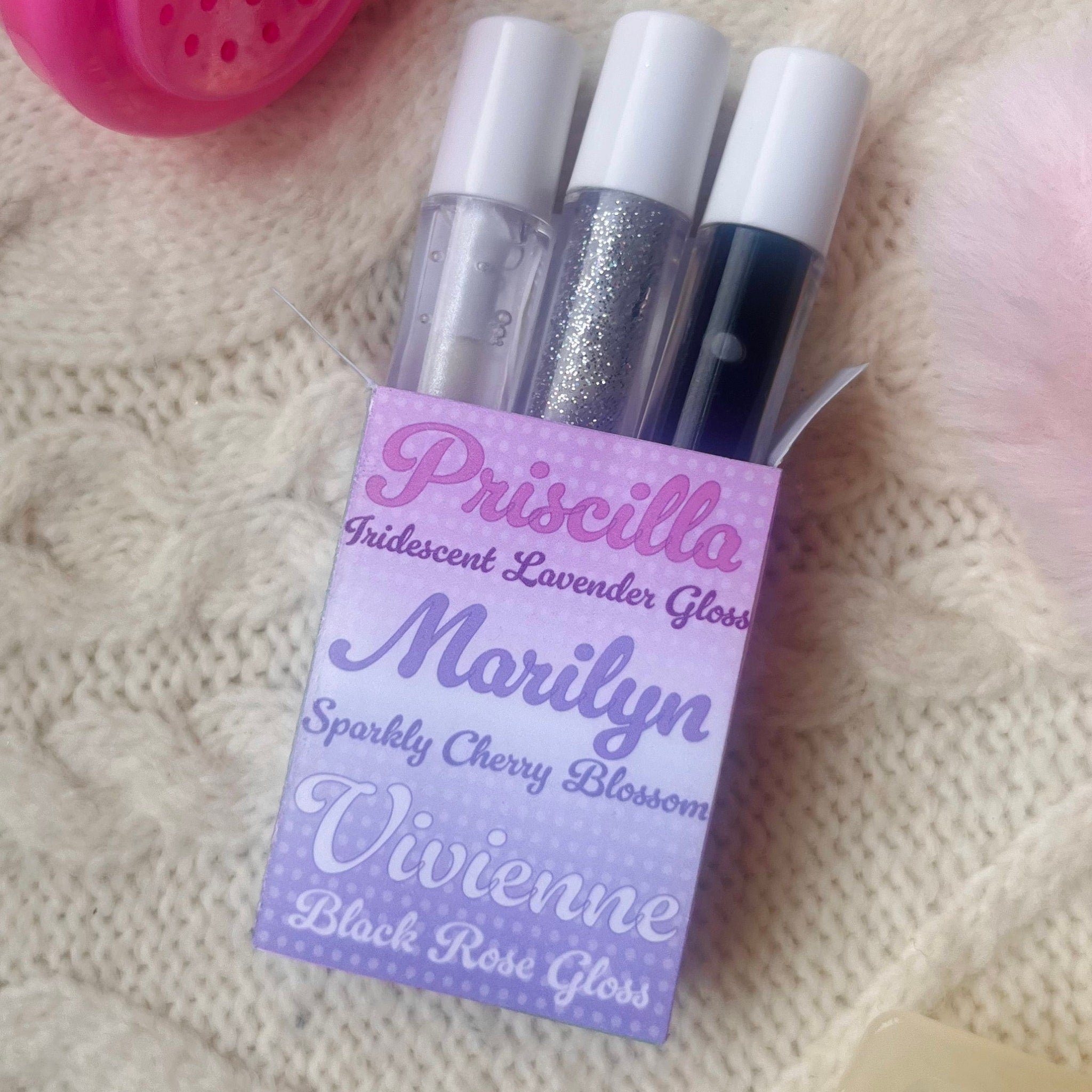 Lip gloss tubes with clear, silver glitter, and black gloss, in a Lars Cosmetics box on knit fabric