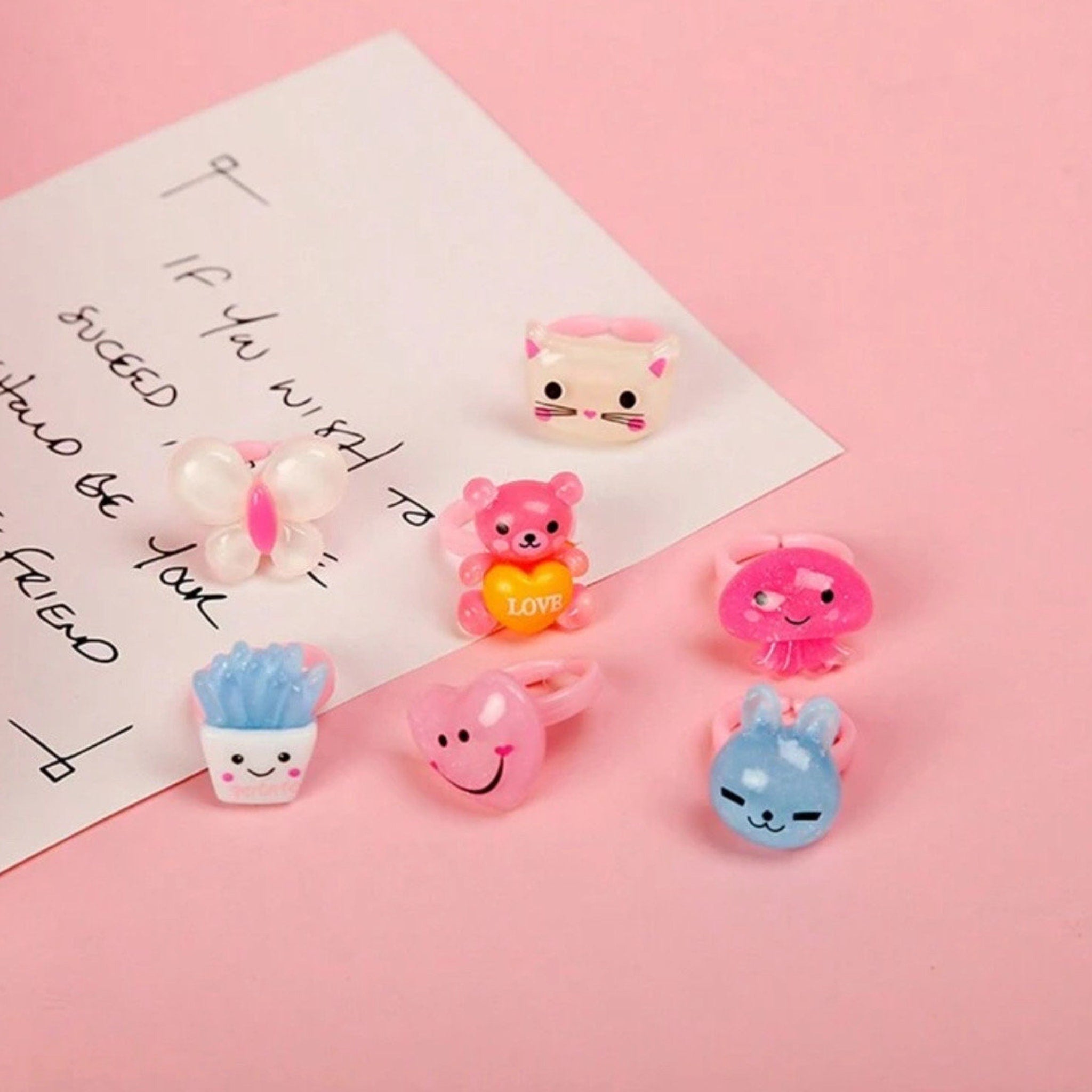 Toy rings in various colors and shapes, including a bear, bunny, and heart, on pink background