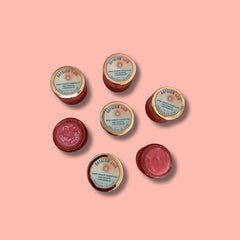 Lip scrub jars, red and gold containers, DAYGLOW SKIN branding visible on the lids, on a pink background