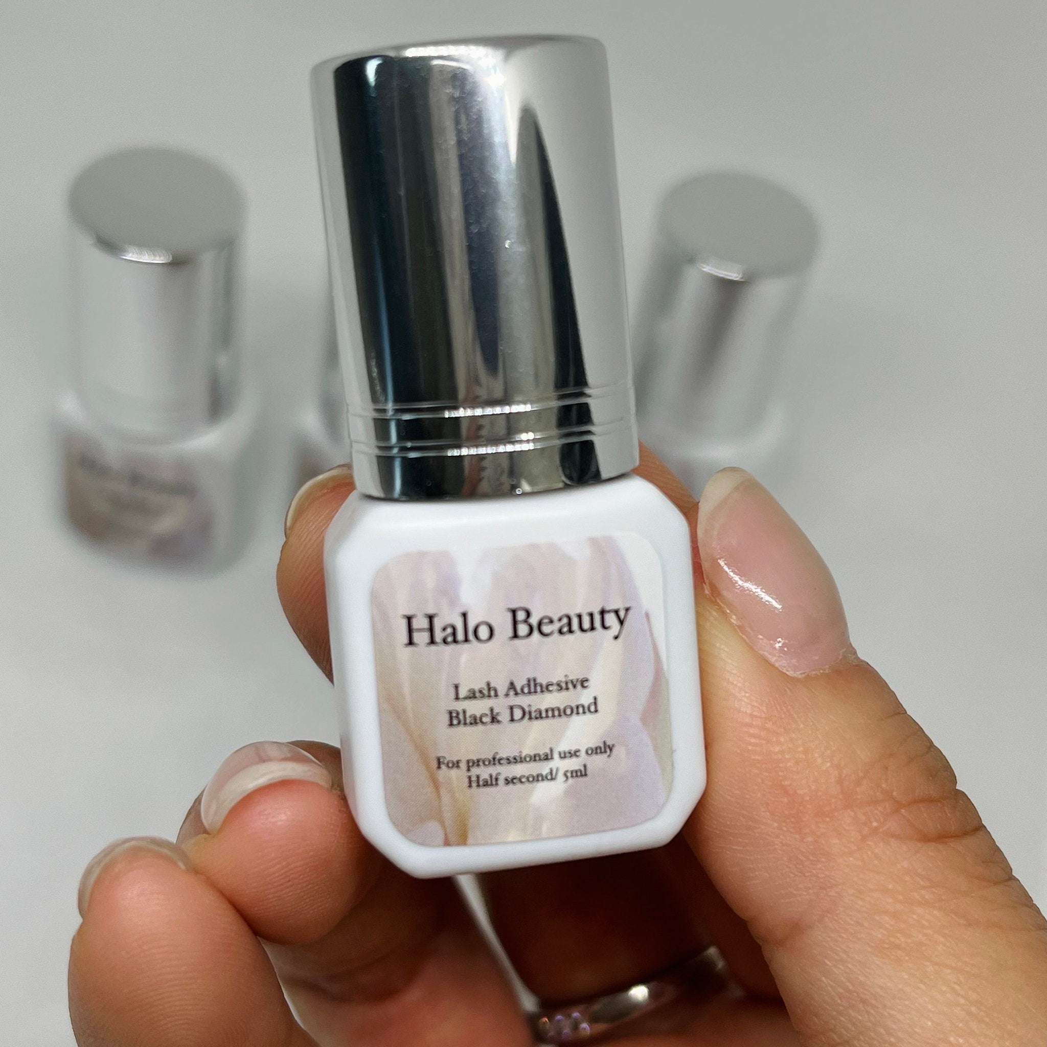 Lash adhesive bottle with silver cap, white label, and Halo Beauty text, held by hand