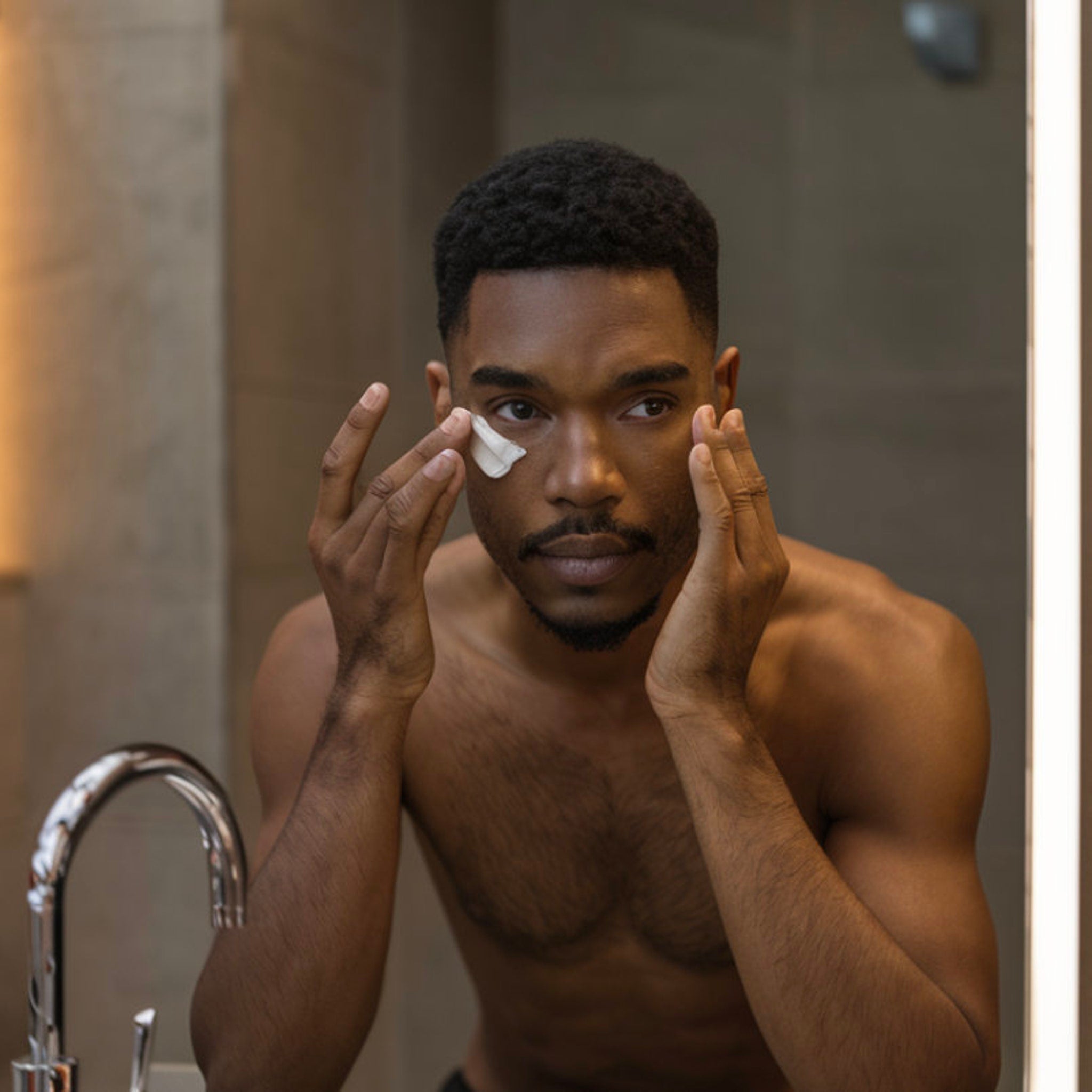 Facial cream application with white cream on face, dark skin, in bathroom setting