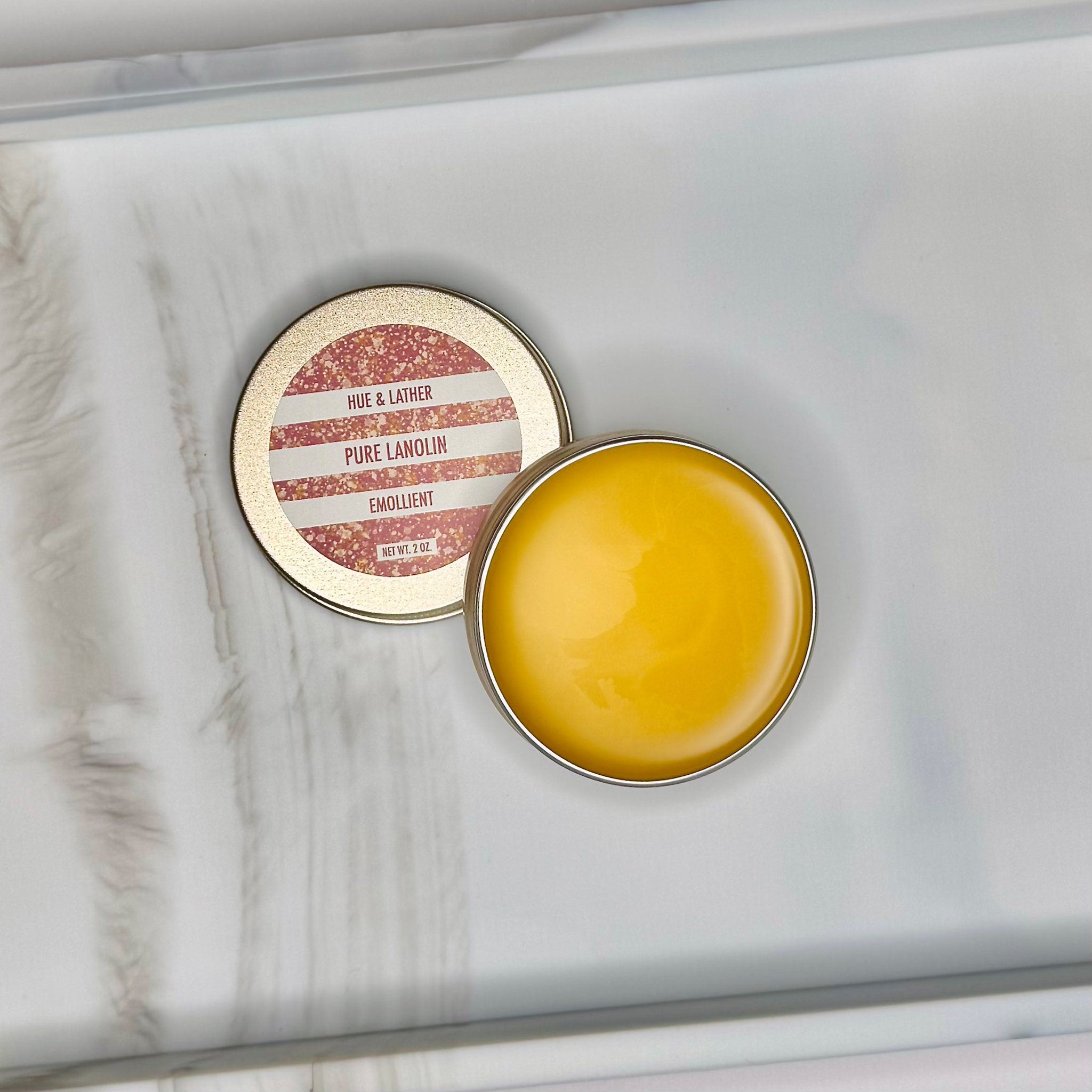 Lanolin balm in a gold tin with yellow emollient and brand name "HUE & LATHER" visible