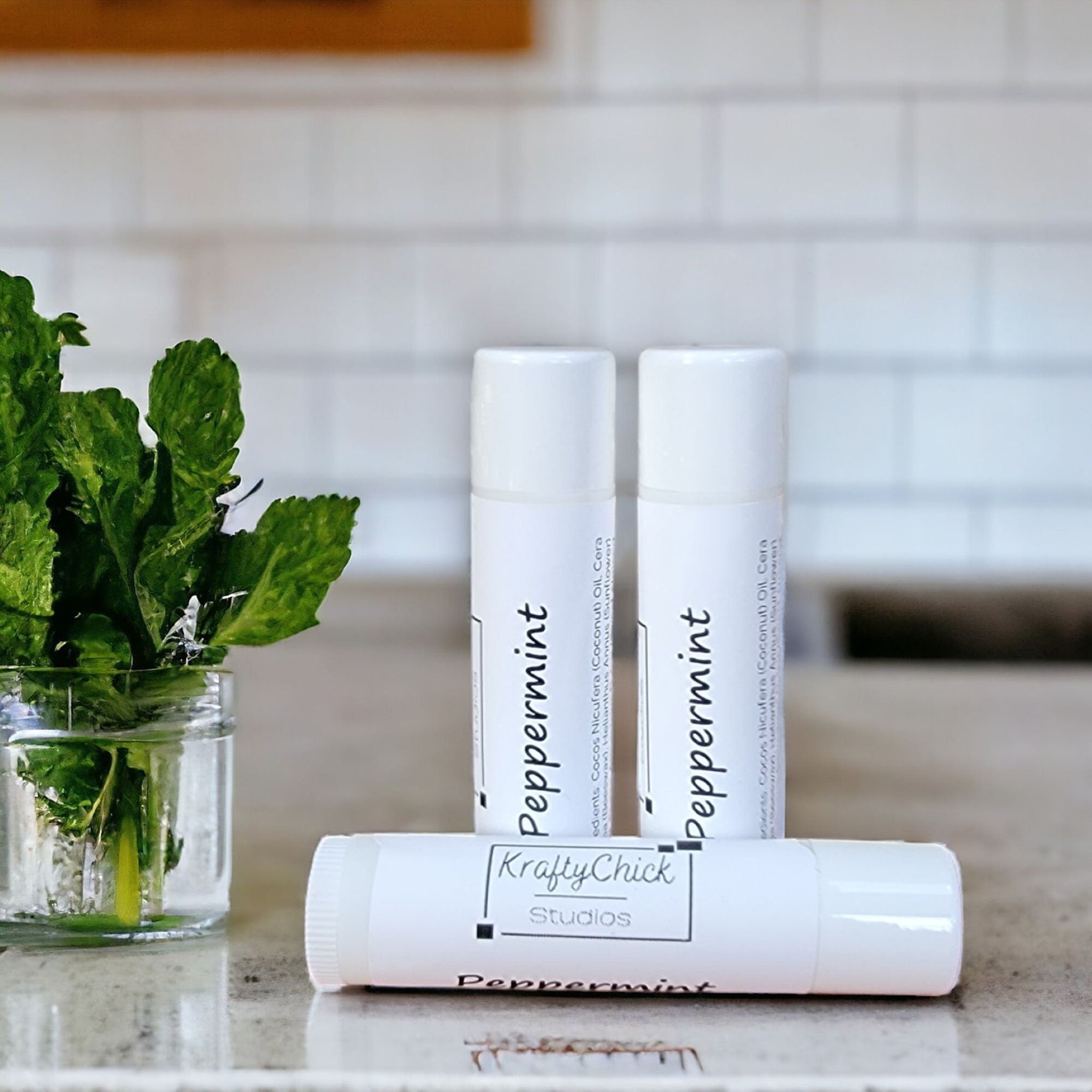 Peppermint lip balm tubes, white with black text, KraftyChickStudios branding, on a counter