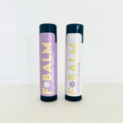 Lip balm tubes with black caps and colorful labels featuring F*BALM branding and flavor text