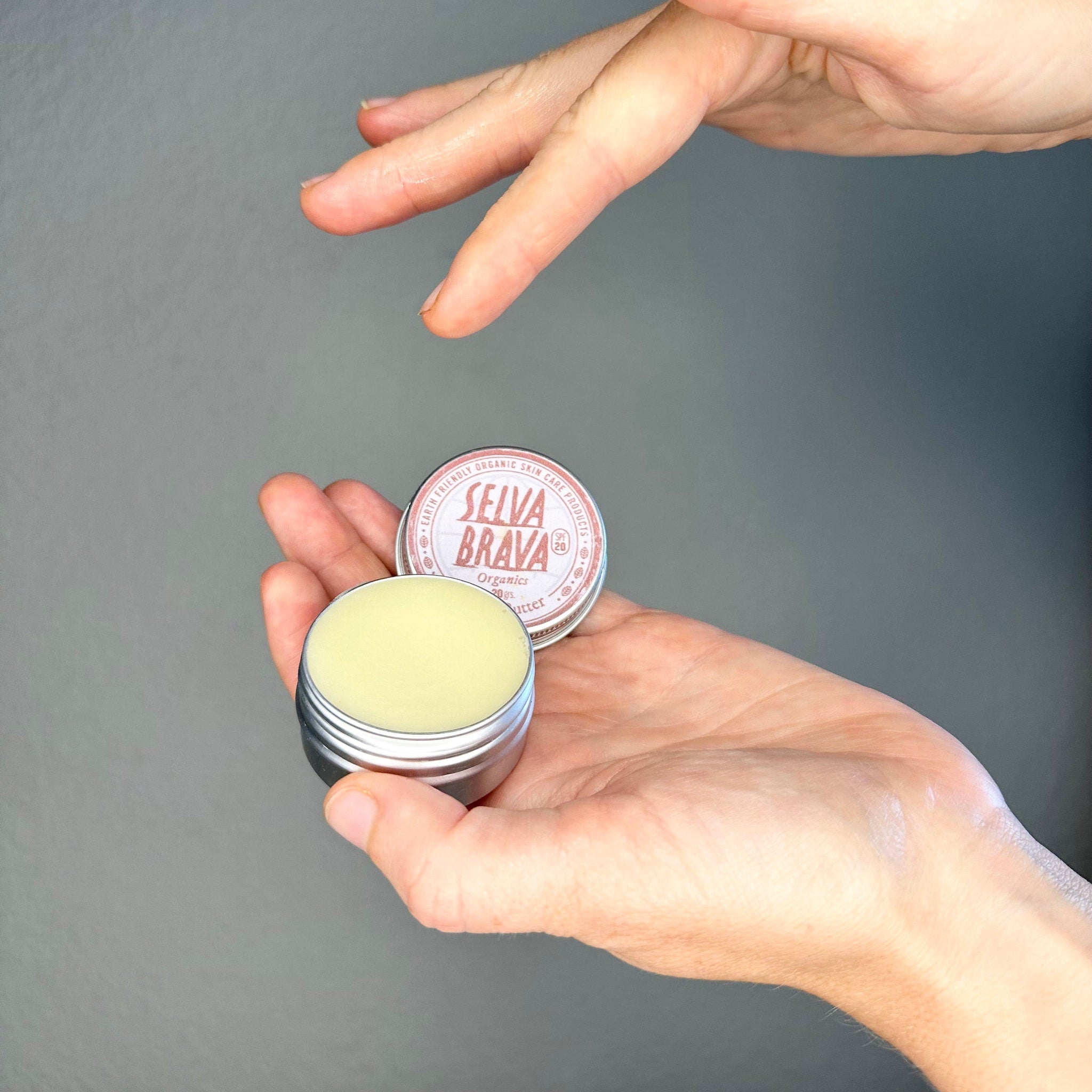 Skin butter in silver tin with yellow balm, held in hands, Selva Brava brand visible