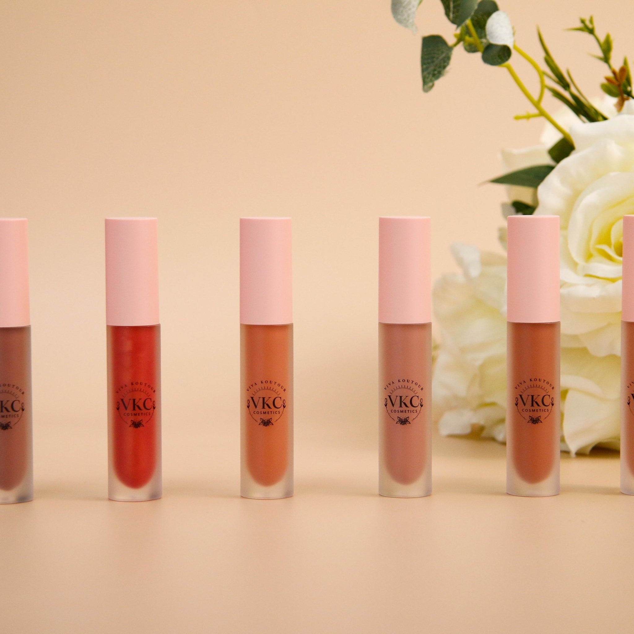 Lipstick tubes with pink caps and various shades of color, VKC Cosmetics brand visible on tubes