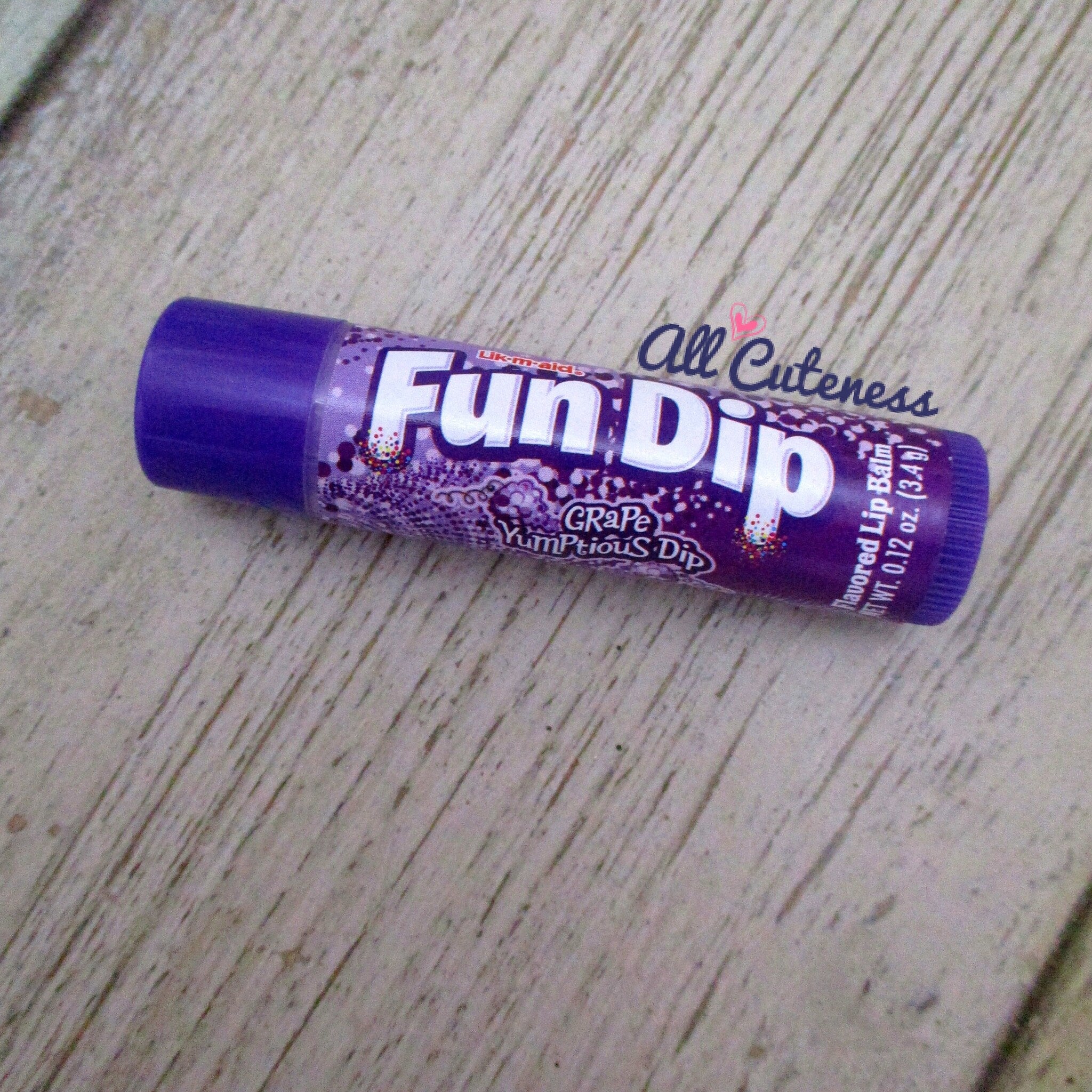 Lip balm tube with purple and white Fun Dip branding on wooden surface