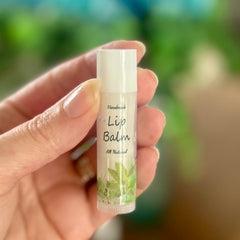 Lip balm tube with white cap, clear tube, and green leaf design held by hand
