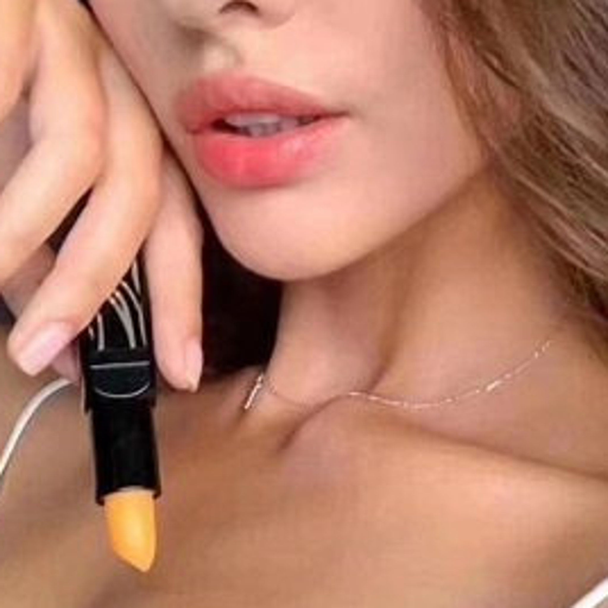 Lip balm with black tube and orange balm, held near lips