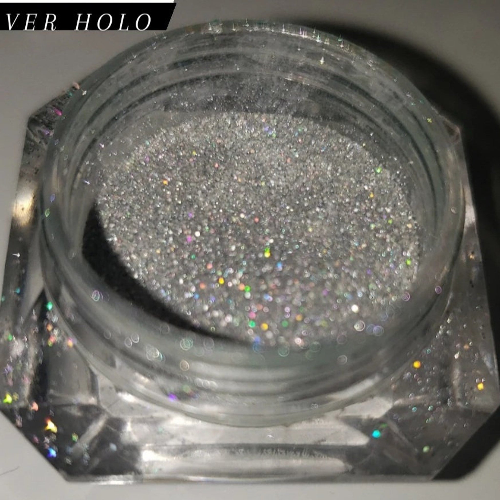 Close-up of shimmering loose glitter eye shadow in a sleek transparent jar with gold lid, showcasing vibrant sparkle particles.