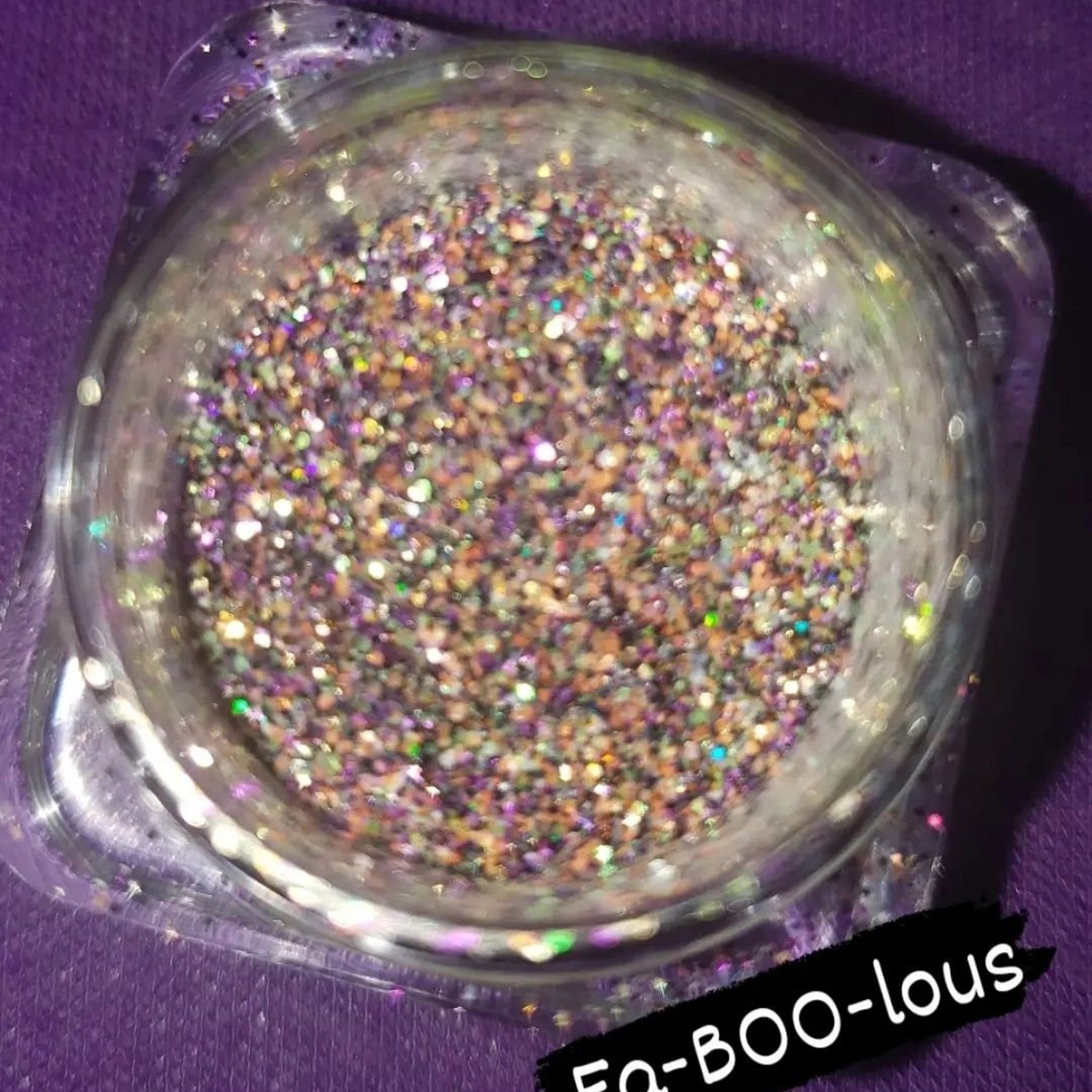 Side view of shimmering loose glitter eye shadow in a sleek transparent jar with gold lid, showcasing fine sparkle texture