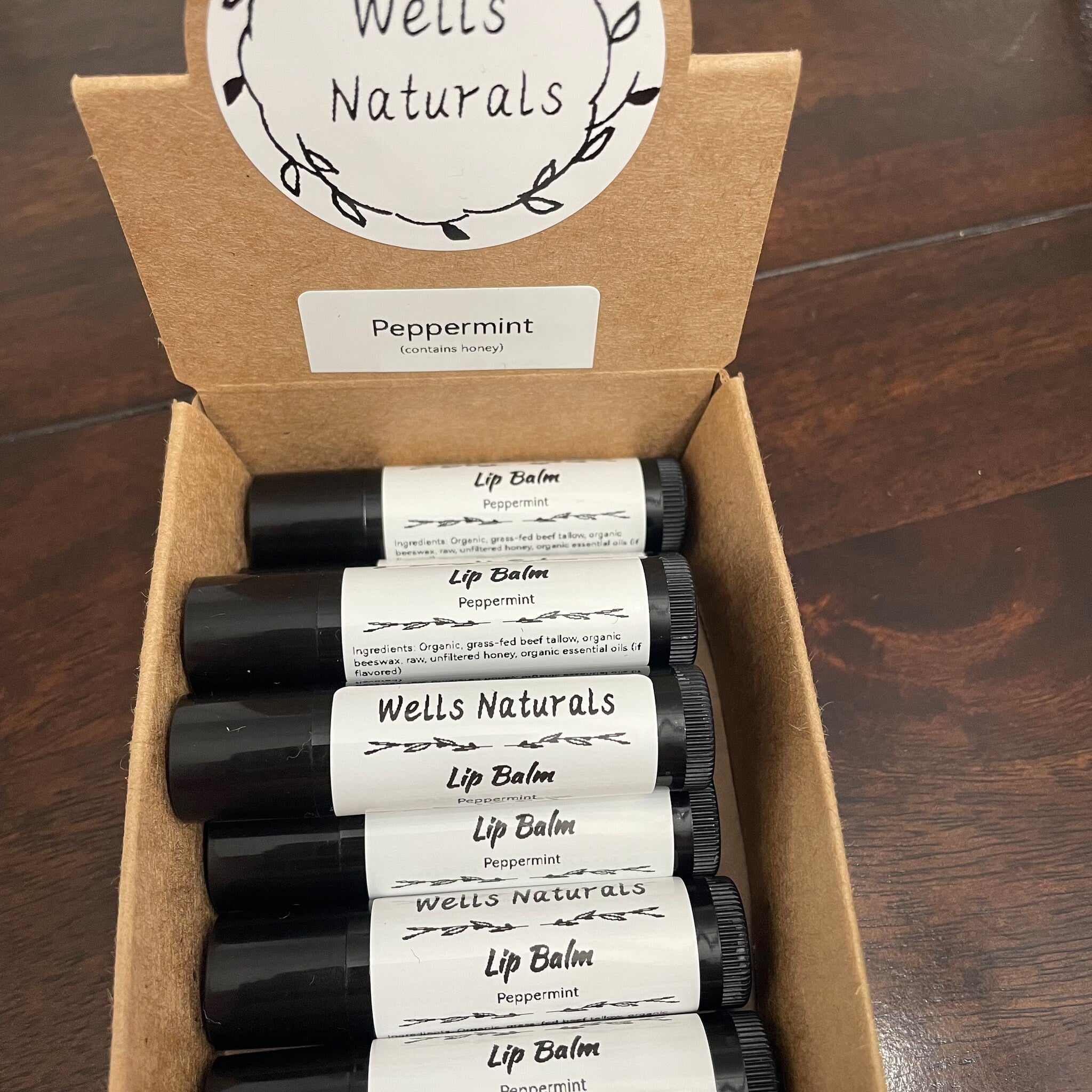 Lip balm tubes with black and white labels in a brown cardboard box, Wells Naturals brand