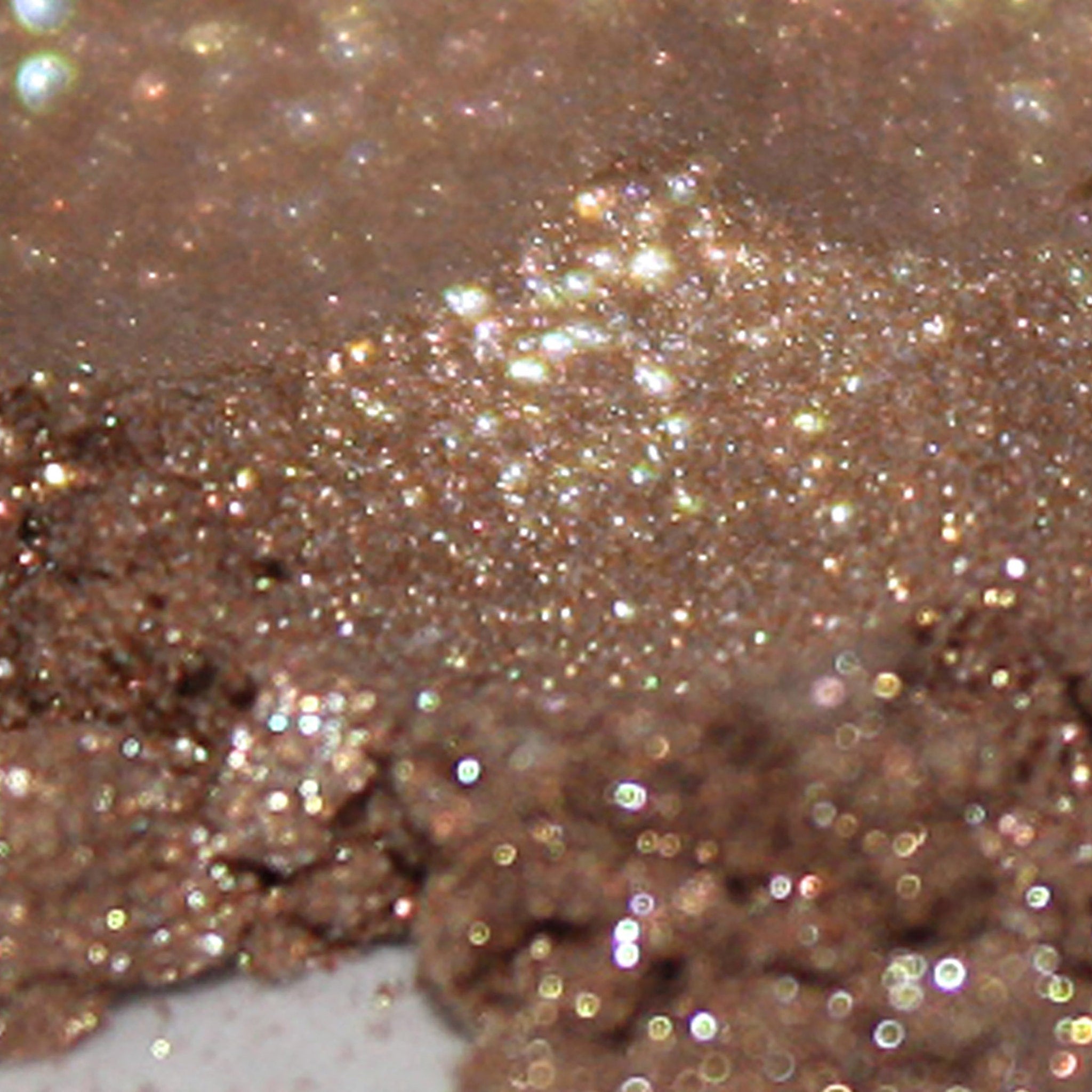 Side view of golden brown loose powder eyeshadow with gold duochrome and silver glitter particles shimmering