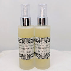 Rosewater toner bottles with clear spray tops, yellow liquid, and decorative labels.