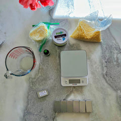 Candle making supplies with clear bags, white scale, and "DIGNITY" jar on marble surface