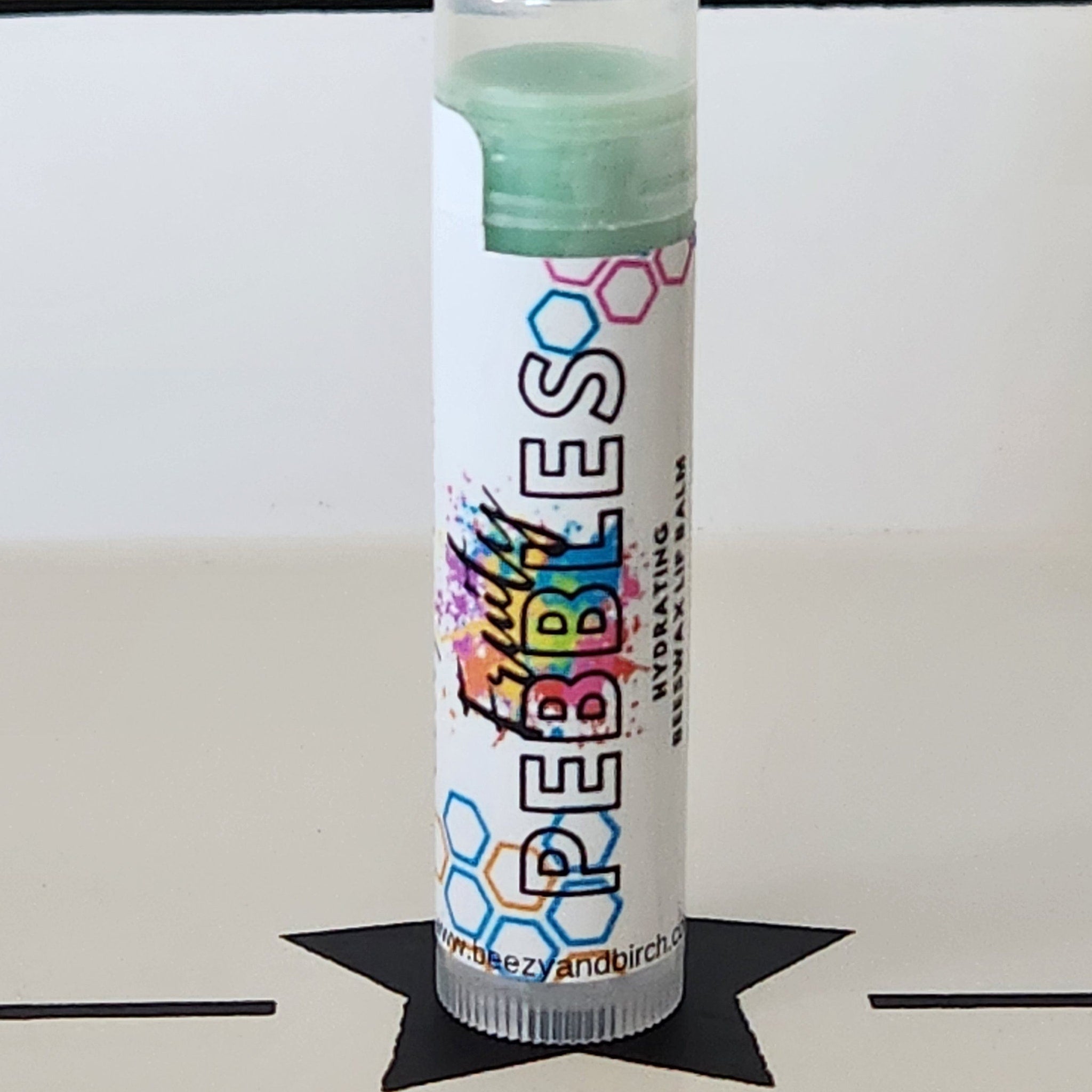 Lip balm tube with green balm, white label, and colorful "PEEBEEES" brand text