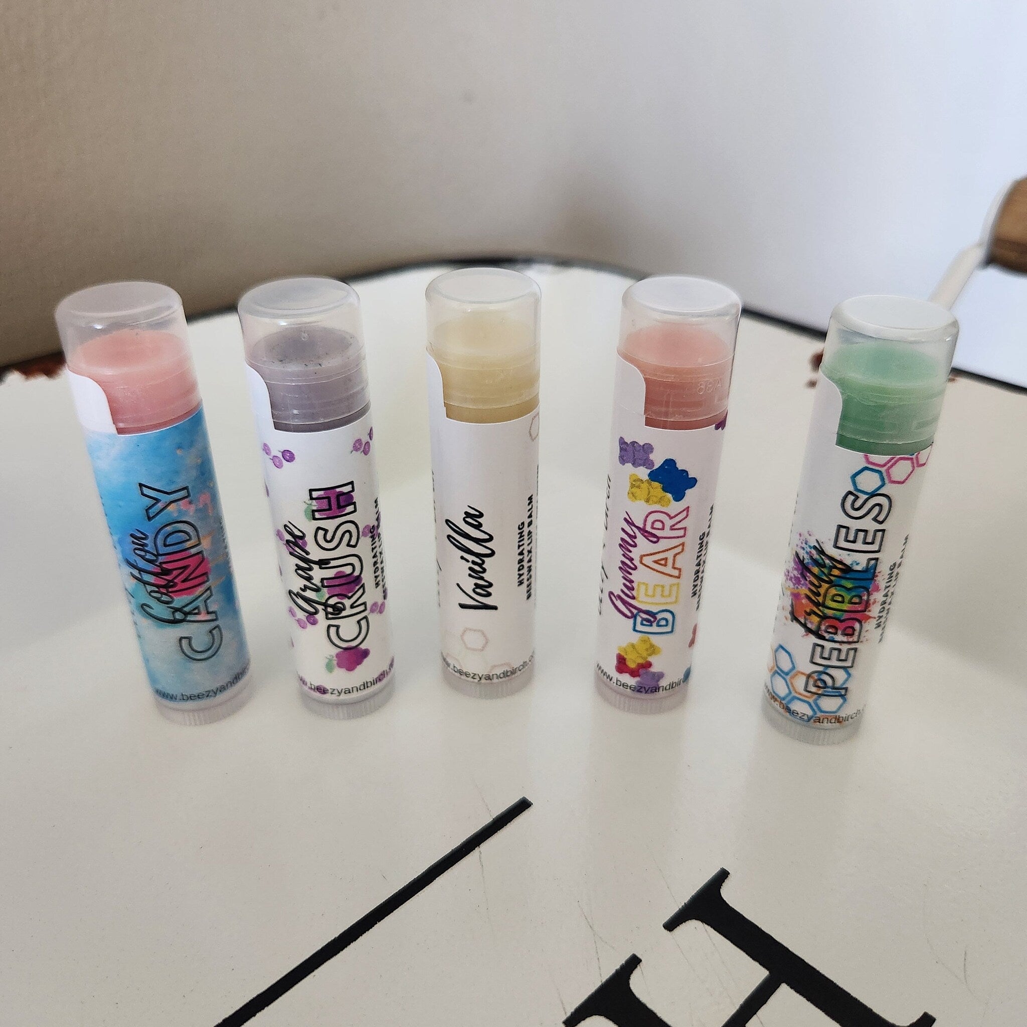 Lip balm tubes in various colors with printed labels, clear caps, and text "Candy" and "Grape Crush" visible