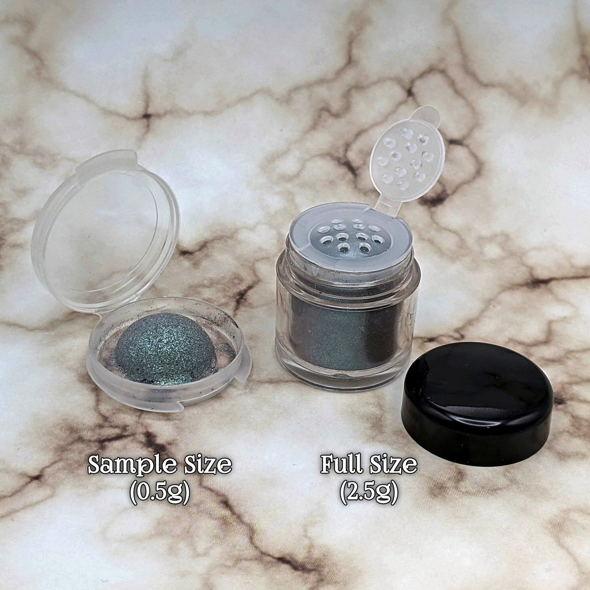 Eyeshadow samples in clear and black containers with metallic green pigment, marble background