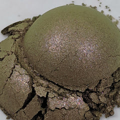 Side view of loose powder eye shadow in deep olive green and copper duochrome, showcasing shimmer particles in jar.