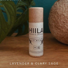Lip balm tube with brown cap and HIILA label, on wooden surface, with plant in background