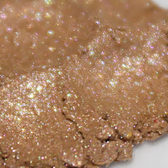 Side view of loose powder eyeshadow in rose gold shimmer with peach and pink tones, showing texture