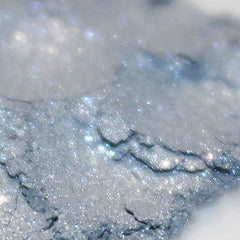 Side view of loose powder vegan eye shadow in pale silver blue with sparkle particles, showcasing texture and shine