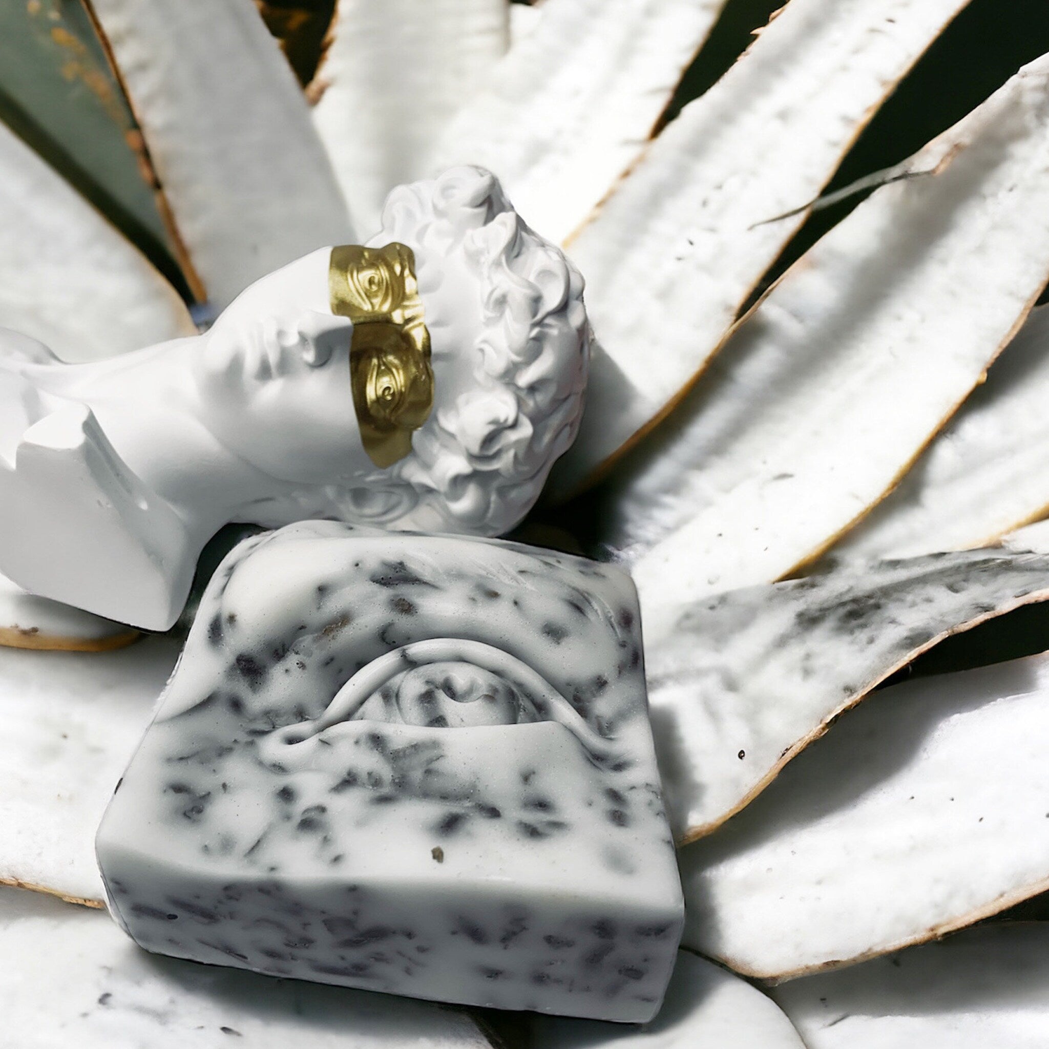 Soap bar with black and white pattern, eye design, and white bust with gold accents on white leaves