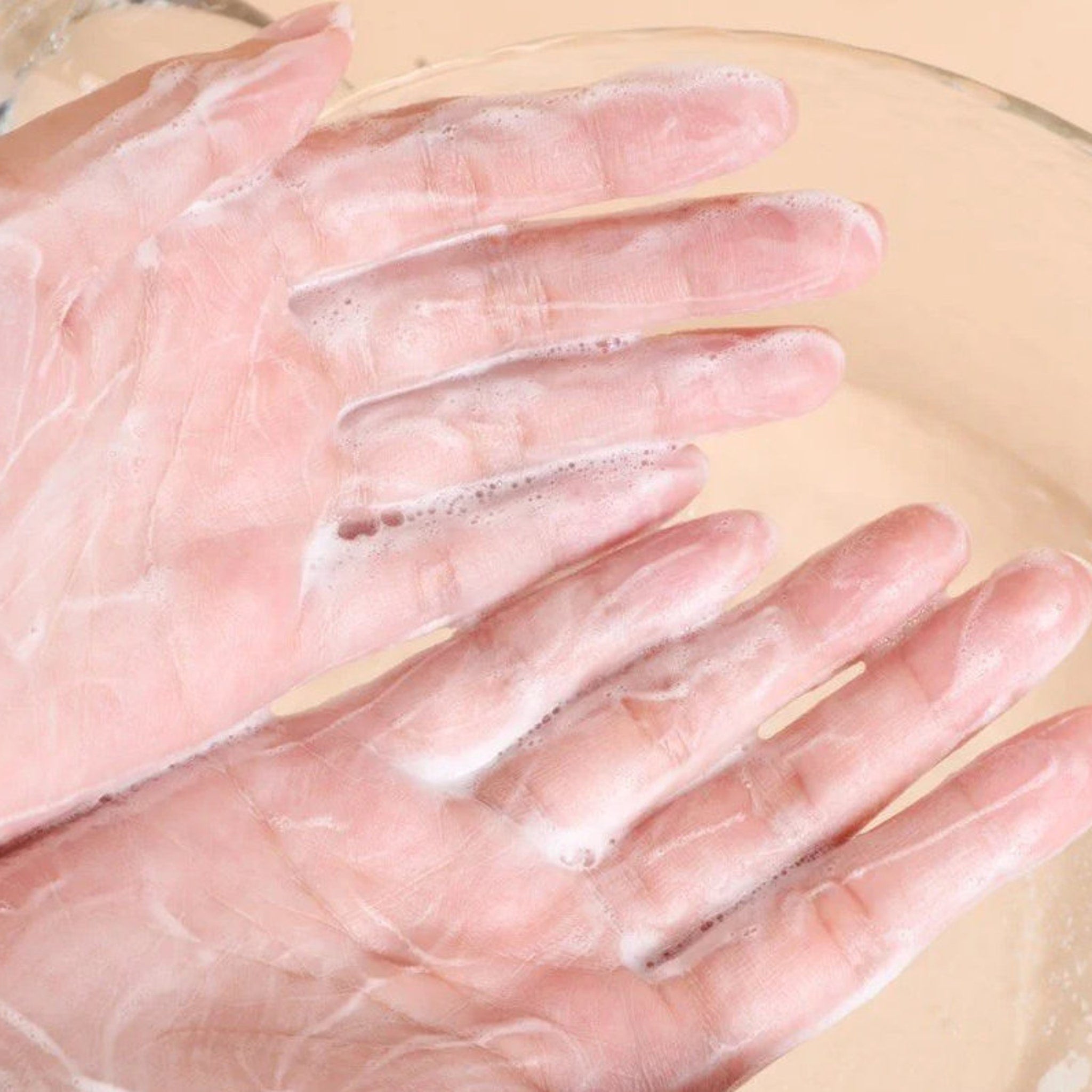 Hands with pink skin and white foam, washing in a clear bowl