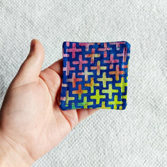 Square fabric with blue background, colorful cross pattern, and stitched edges held in hand