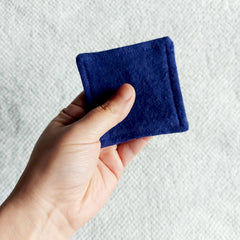 Reusable facial pad, navy blue felt square held in hand, showing stitched edge detail