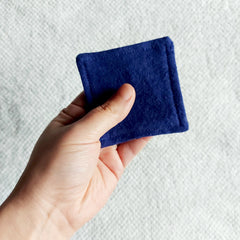Square blue felt pad held in hand, showing texture and stitched edge