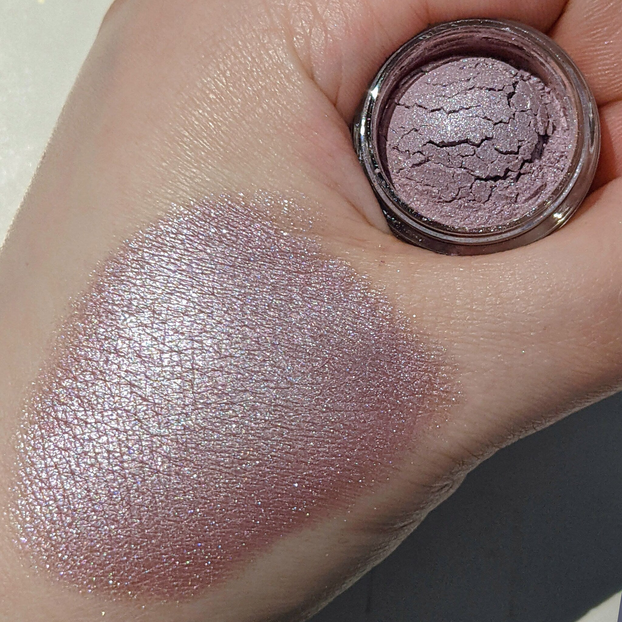 Eyeshadow swatch with mauve shimmer and cracked texture shown on skin next to jar