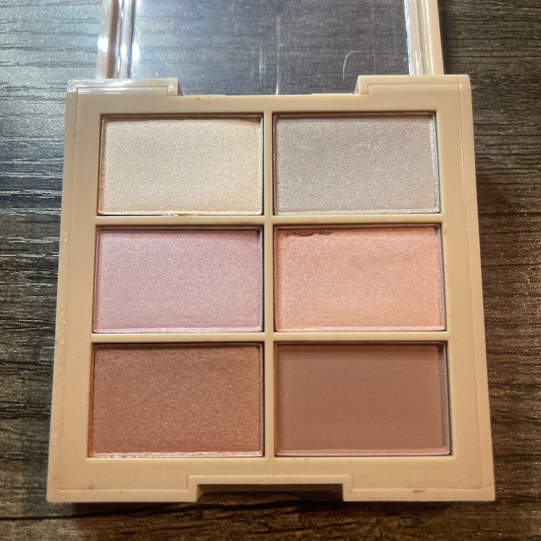 Eyeshadow palette with neutral shades of pink, beige, and brown in a square compact
