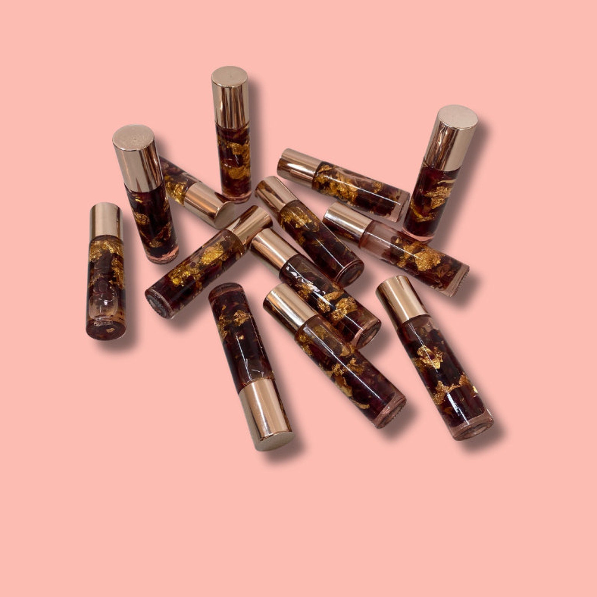 Roller bottles with gold caps, clear glass, and gold flakes, arranged on pink background
